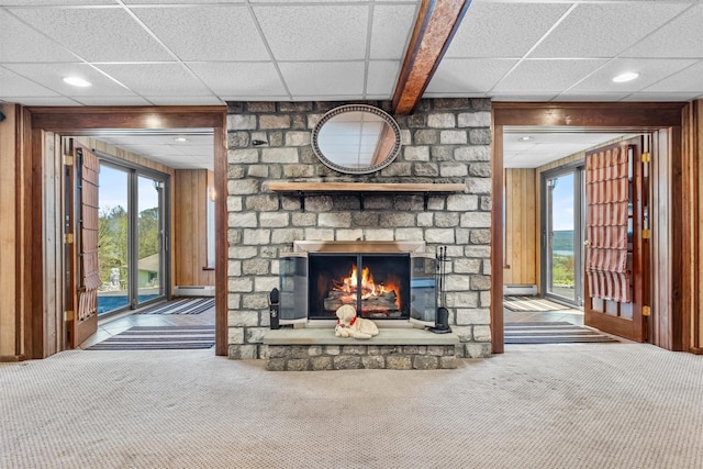 unfurnished living room featuring wooden walls, a large fireplace, a paneled ceiling, and carpet