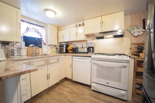 kitchen with decorative backsplash, a sink, light countertops, under cabinet range hood, and white appliances