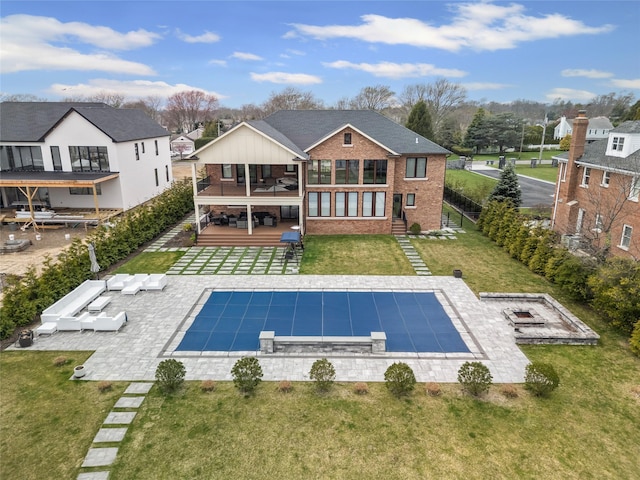 rear view of house featuring a covered pool, brick siding, a patio area, a balcony, and a lawn