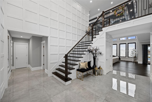 stairway featuring baseboards, a high ceiling, a decorative wall, and recessed lighting