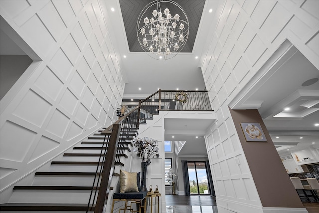foyer featuring a high ceiling, a decorative wall, a chandelier, stairs, and ornamental molding