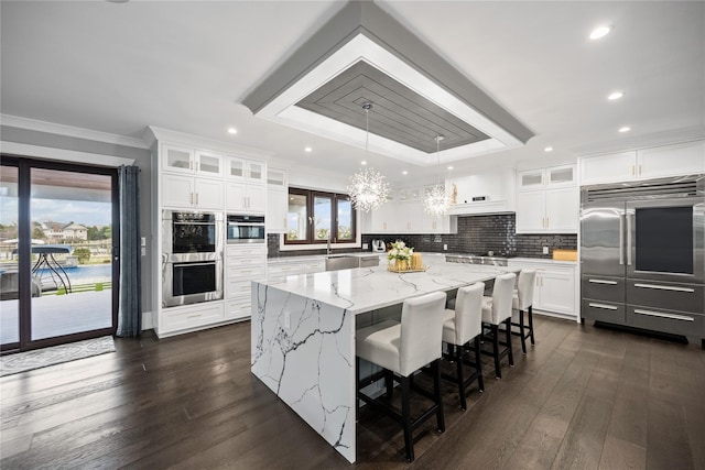 kitchen featuring a notable chandelier, appliances with stainless steel finishes, a center island, a tray ceiling, and glass insert cabinets