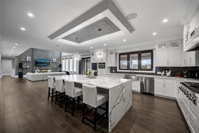 kitchen featuring appliances with stainless steel finishes, a sink, light stone counters, an inviting chandelier, and a tray ceiling