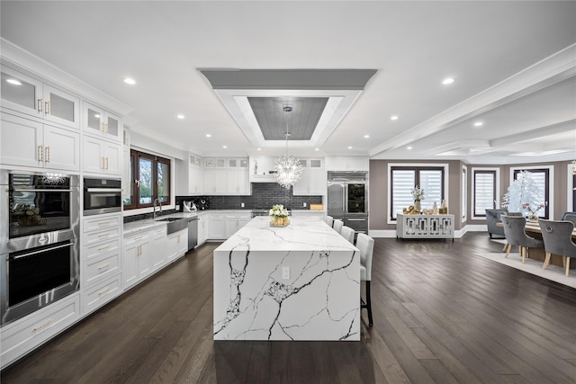 kitchen with dark wood-style flooring, appliances with stainless steel finishes, light stone counters, a raised ceiling, and decorative backsplash