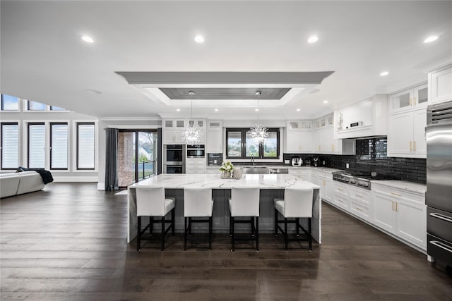 kitchen featuring a sink, a raised ceiling, a center island, stainless steel appliances, and white cabinetry