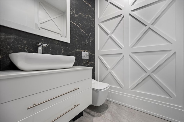 bathroom with toilet, wallpapered walls, marble finish floor, and vanity