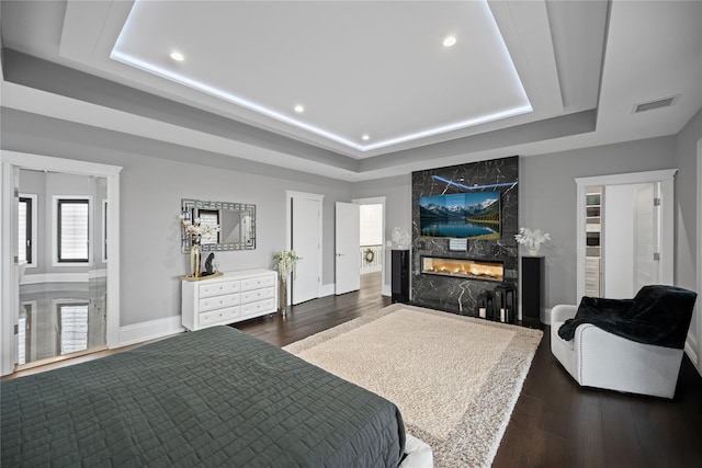 bedroom featuring a high end fireplace, a raised ceiling, dark wood-style flooring, and visible vents