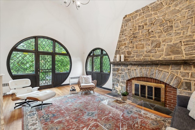 living room featuring wood-type flooring, radiator heating unit, a towering ceiling, and a large fireplace