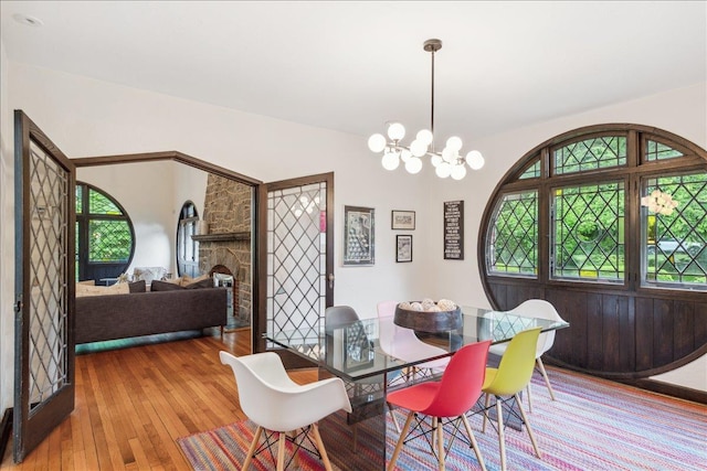 dining room with hardwood / wood-style flooring, a chandelier, and a stone fireplace