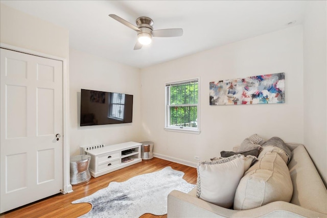 living area with a ceiling fan, wood finished floors, and baseboards