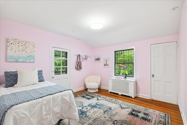 bedroom featuring multiple windows, radiator heating unit, wood finished floors, baseboards, and vaulted ceiling