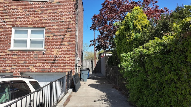 view of side of home featuring fence, a garage, and brick siding