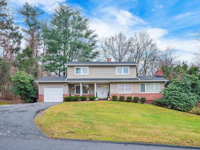 traditional home featuring driveway, a chimney, a front yard, a garage, and brick siding