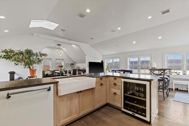kitchen with beverage cooler, visible vents, a sink, and vaulted ceiling with skylight