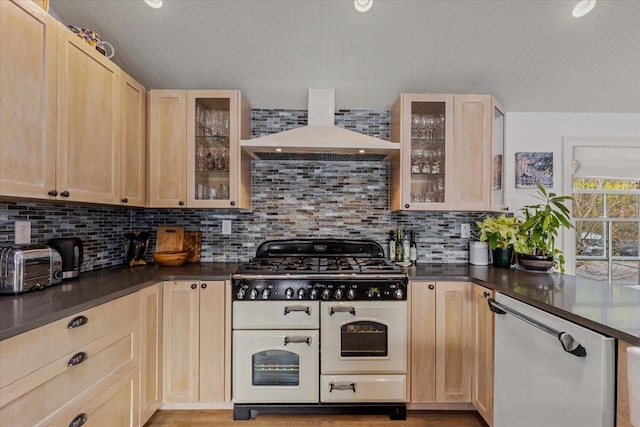kitchen with light brown cabinets, dark countertops, wall chimney exhaust hood, tasteful backsplash, and double oven range