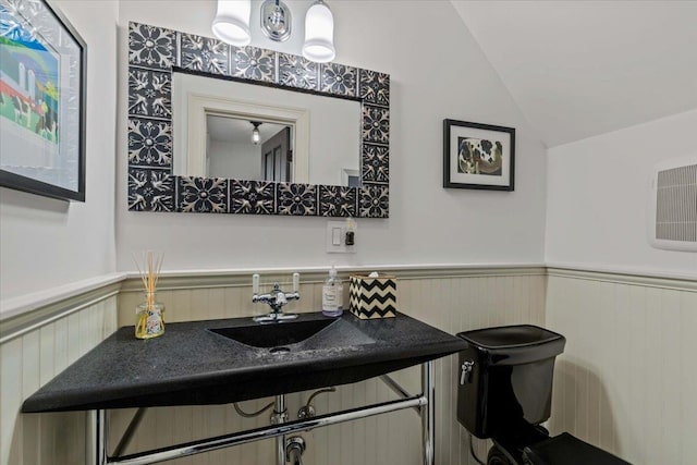 half bath with vanity, a wainscoted wall, vaulted ceiling, and toilet