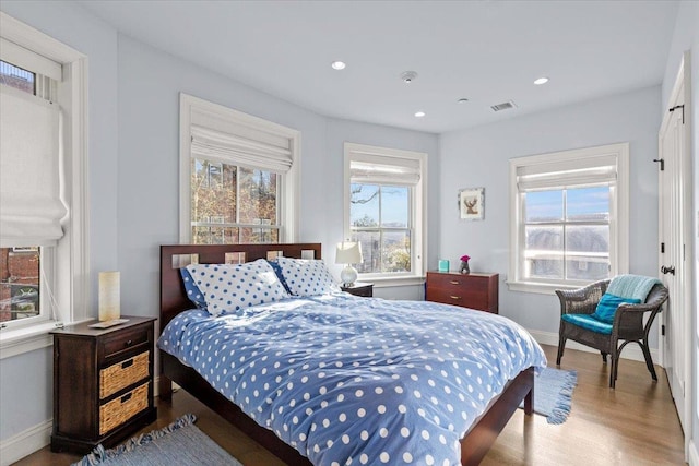 bedroom with baseboards, visible vents, multiple windows, and wood finished floors
