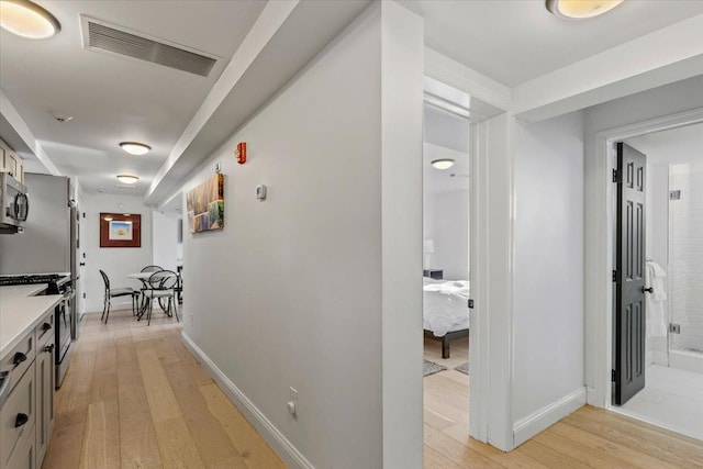 hallway with baseboards, light wood-style flooring, and visible vents