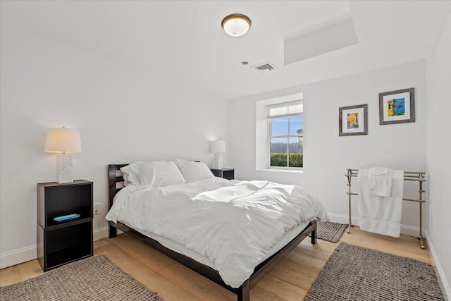 bedroom featuring baseboards, light wood-type flooring, a raised ceiling, and visible vents