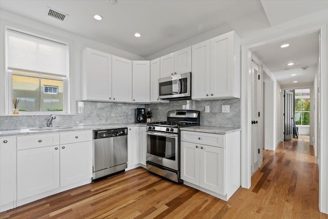 kitchen with appliances with stainless steel finishes, tasteful backsplash, light wood finished floors, and visible vents
