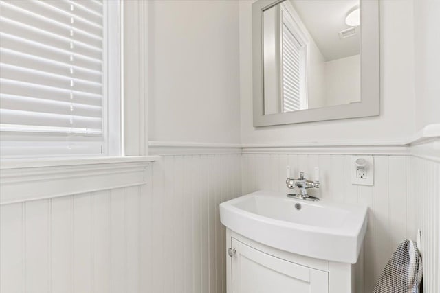 bathroom featuring vanity, wainscoting, a decorative wall, and visible vents