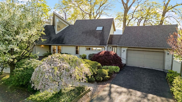 cape cod-style house featuring an attached garage, a shingled roof, and driveway