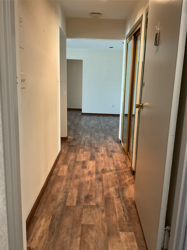 hallway featuring dark wood-style flooring and baseboards