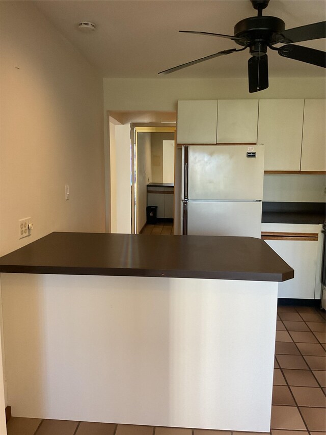 kitchen featuring dark countertops, tile patterned floors, freestanding refrigerator, a ceiling fan, and white cabinetry