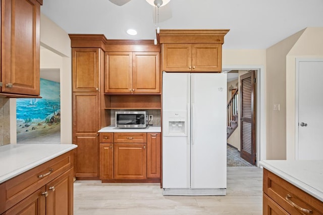 kitchen with light countertops, white refrigerator with ice dispenser, stainless steel microwave, and brown cabinetry