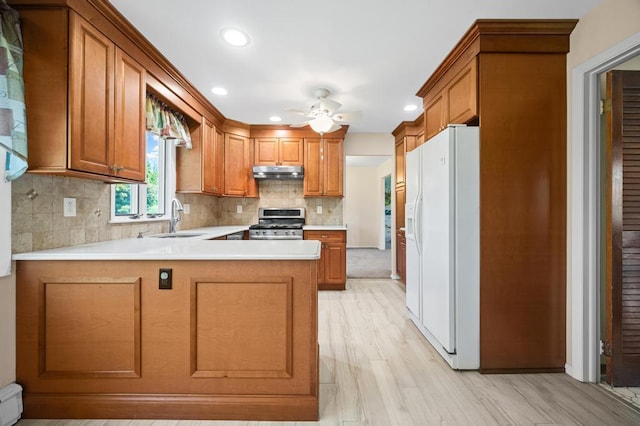 kitchen with white refrigerator with ice dispenser, gas range, light countertops, under cabinet range hood, and a sink