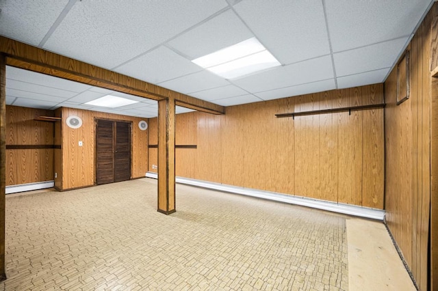 finished basement with a paneled ceiling, baseboard heating, and wooden walls