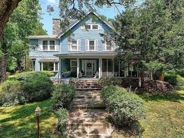view of front of home featuring covered porch, a chimney, and a front lawn