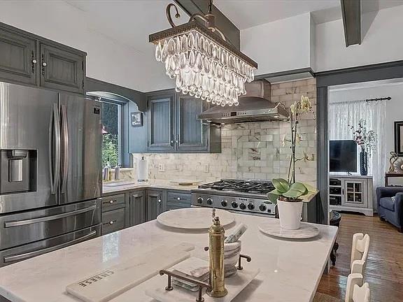 kitchen with backsplash, arched walkways, light stone counters, ventilation hood, and stainless steel fridge