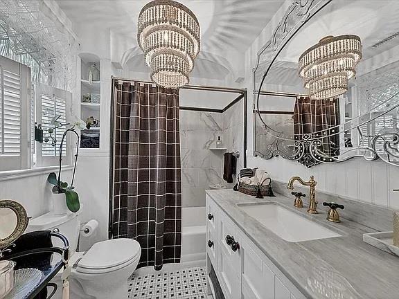 full bath featuring vanity, shower / bath combination with curtain, toilet, and a notable chandelier