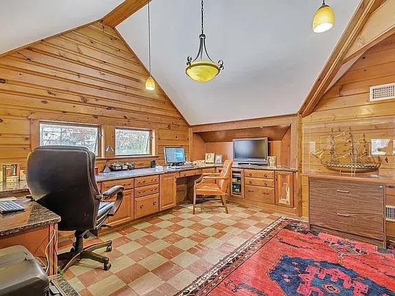 office featuring visible vents, built in desk, lofted ceiling with beams, wooden walls, and light floors