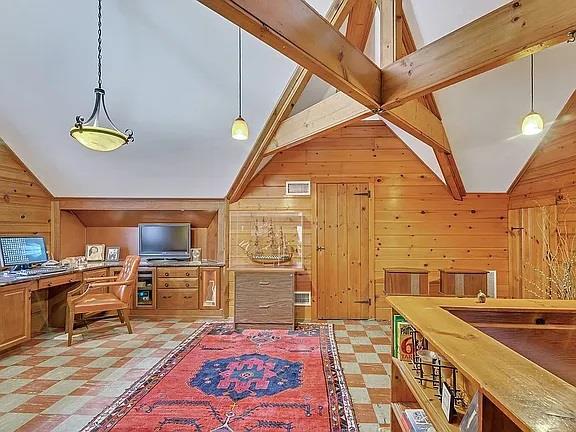 interior space with light floors, vaulted ceiling, wood walls, and visible vents