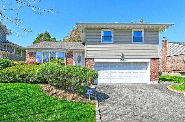 split level home with an attached garage, driveway, a front lawn, and brick siding