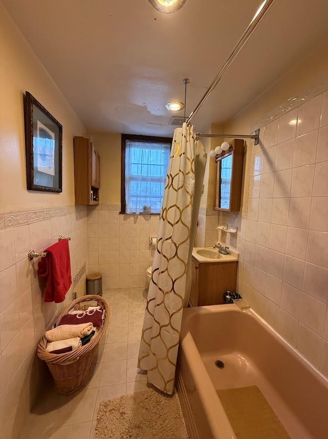 bathroom featuring tile patterned flooring, toilet, tile walls, a sink, and shower / bath combo