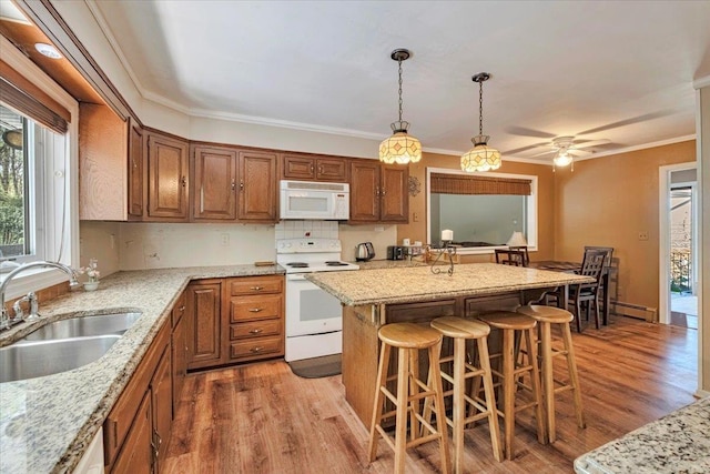 kitchen with a sink, brown cabinets, light wood finished floors, and white appliances