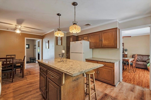 kitchen with crown molding, freestanding refrigerator, a breakfast bar, light wood-style flooring, and decorative light fixtures