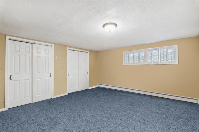 unfurnished bedroom with baseboard heating, a textured ceiling, dark colored carpet, two closets, and baseboards