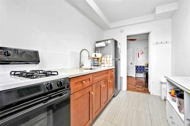 kitchen featuring brown cabinetry, light tile patterned flooring, a raised ceiling, a sink, and gas stove