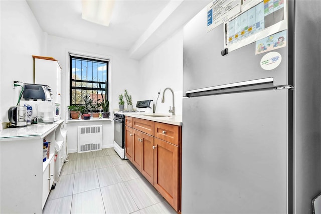 kitchen featuring brown cabinets, a sink, radiator, freestanding refrigerator, and gas range oven