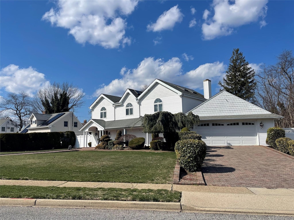 traditional-style home with an attached garage, a chimney, decorative driveway, and a front yard