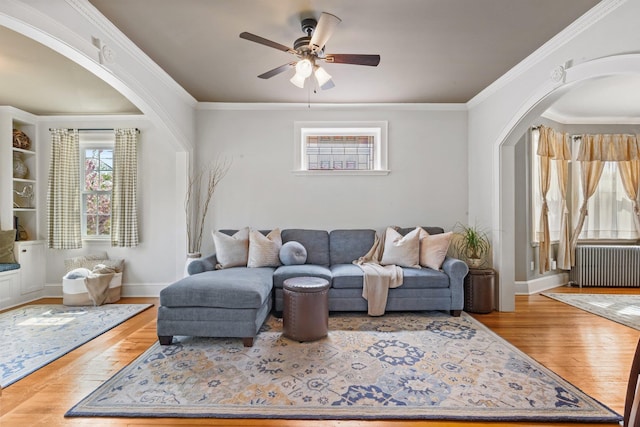 living area featuring a ceiling fan, wood finished floors, baseboards, radiator heating unit, and arched walkways