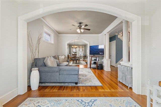 living area featuring arched walkways, a ceiling fan, ornate columns, and radiator heating unit