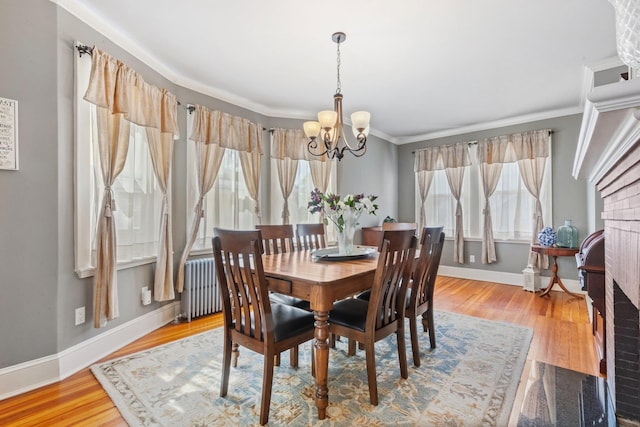 dining room featuring crown molding, wood finished floors, baseboards, a notable chandelier, and radiator heating unit