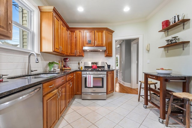 kitchen with backsplash, appliances with stainless steel finishes, brown cabinets, a sink, and under cabinet range hood