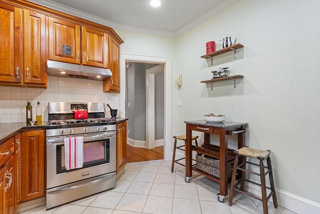 kitchen featuring dark countertops, stainless steel range with gas stovetop, tasteful backsplash, brown cabinets, and under cabinet range hood
