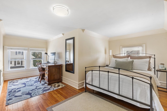 bedroom featuring baseboards, multiple windows, wood finished floors, and ornamental molding